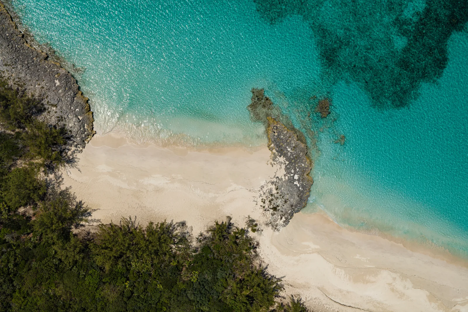 Aerial view of a white-sand cove, rocky outcrop and turquoise shallows