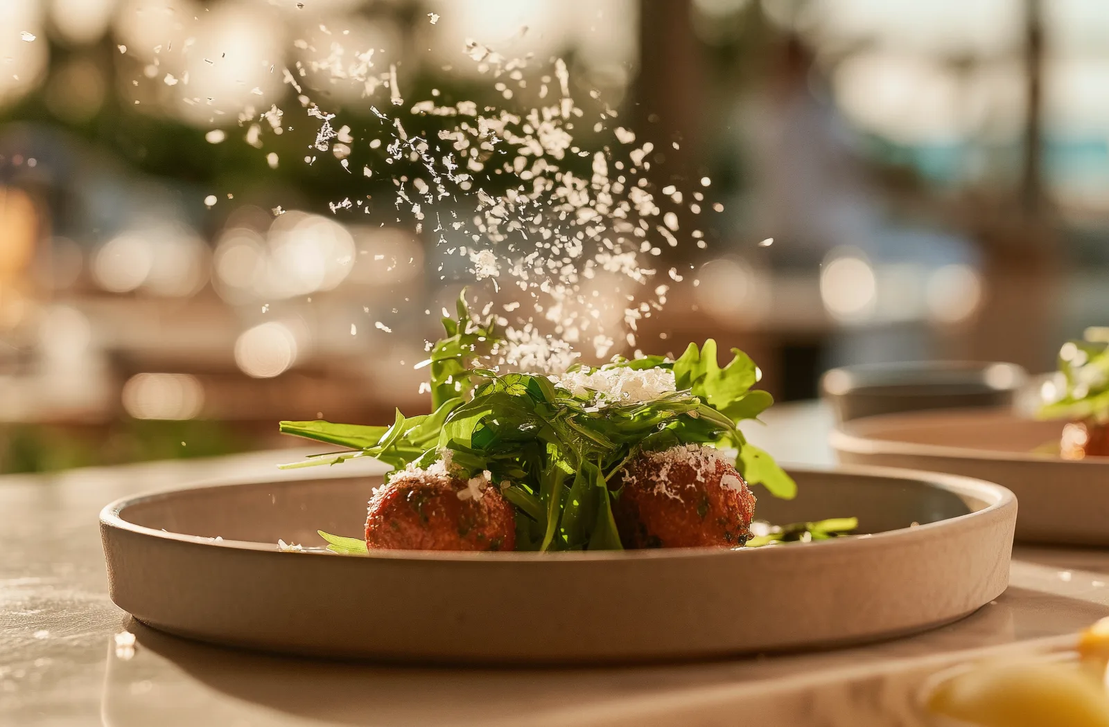 Parmesan falling onto a plated dish on a terrace table