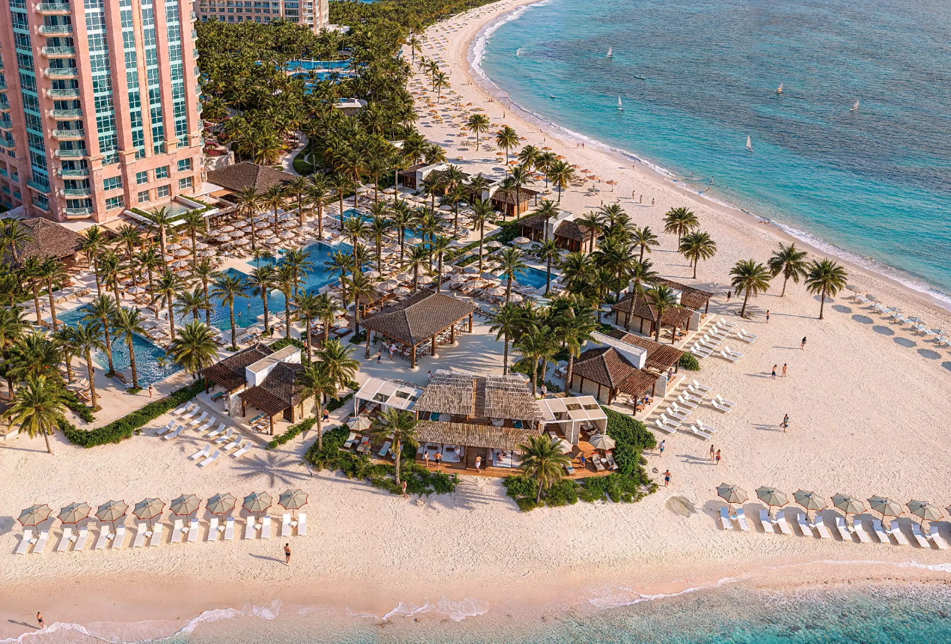 Aerial view of the Beach Club: pools, palms and thatched pavilions along the shore