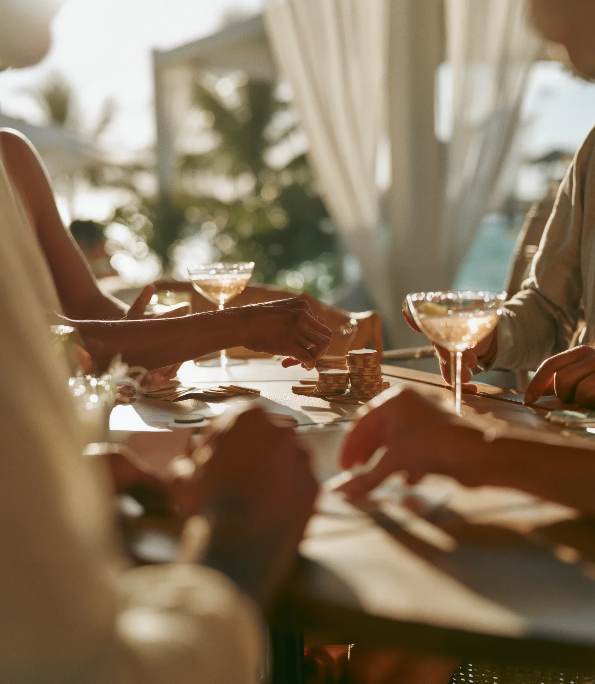 Guests with cocktails around a table in a sunlit, curtained lounge