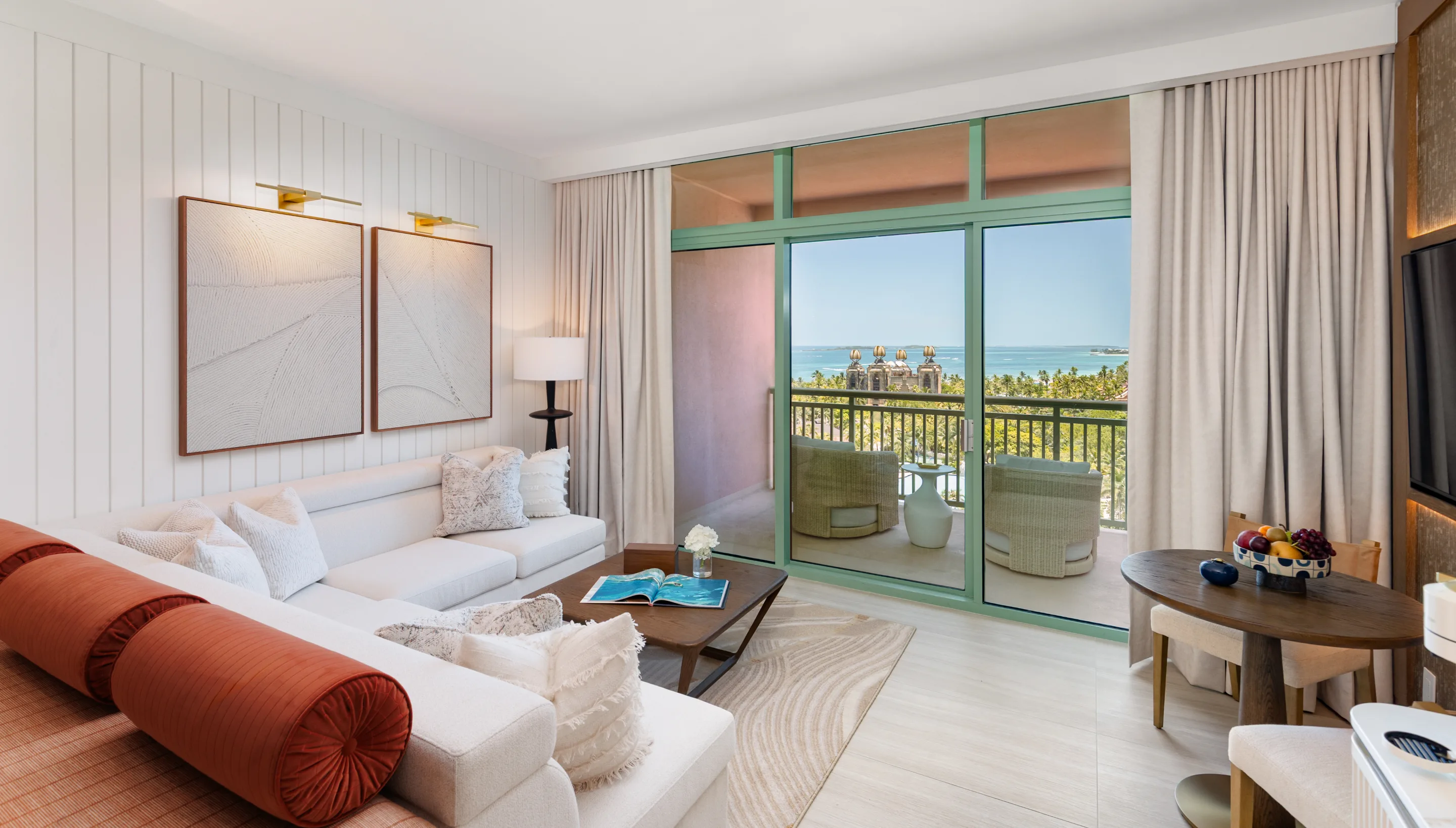 A suite living area: white sofa with coral bolsters, terrace doors open to the ocean