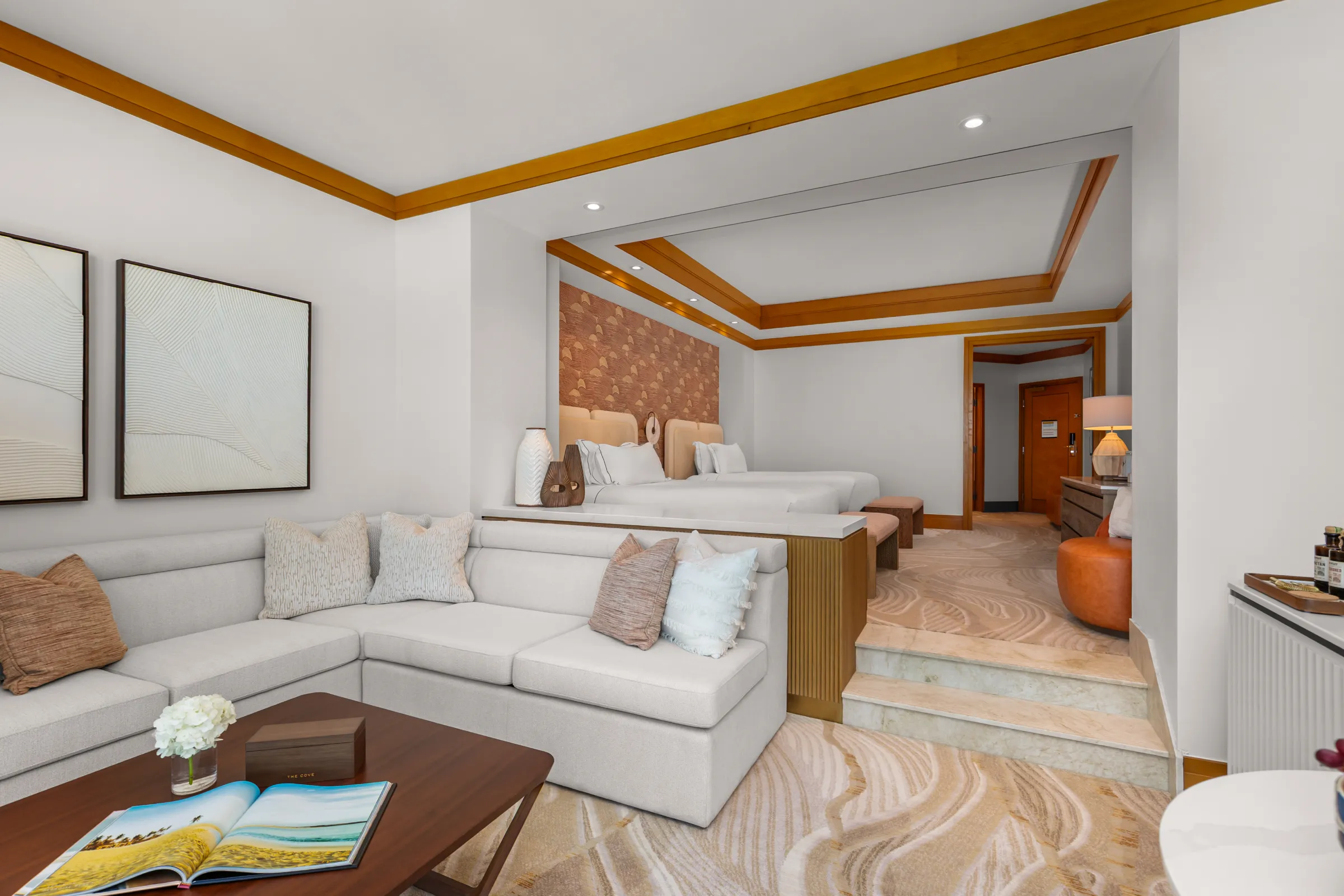 A suite living area with a white sectional and framed art, the beds beyond