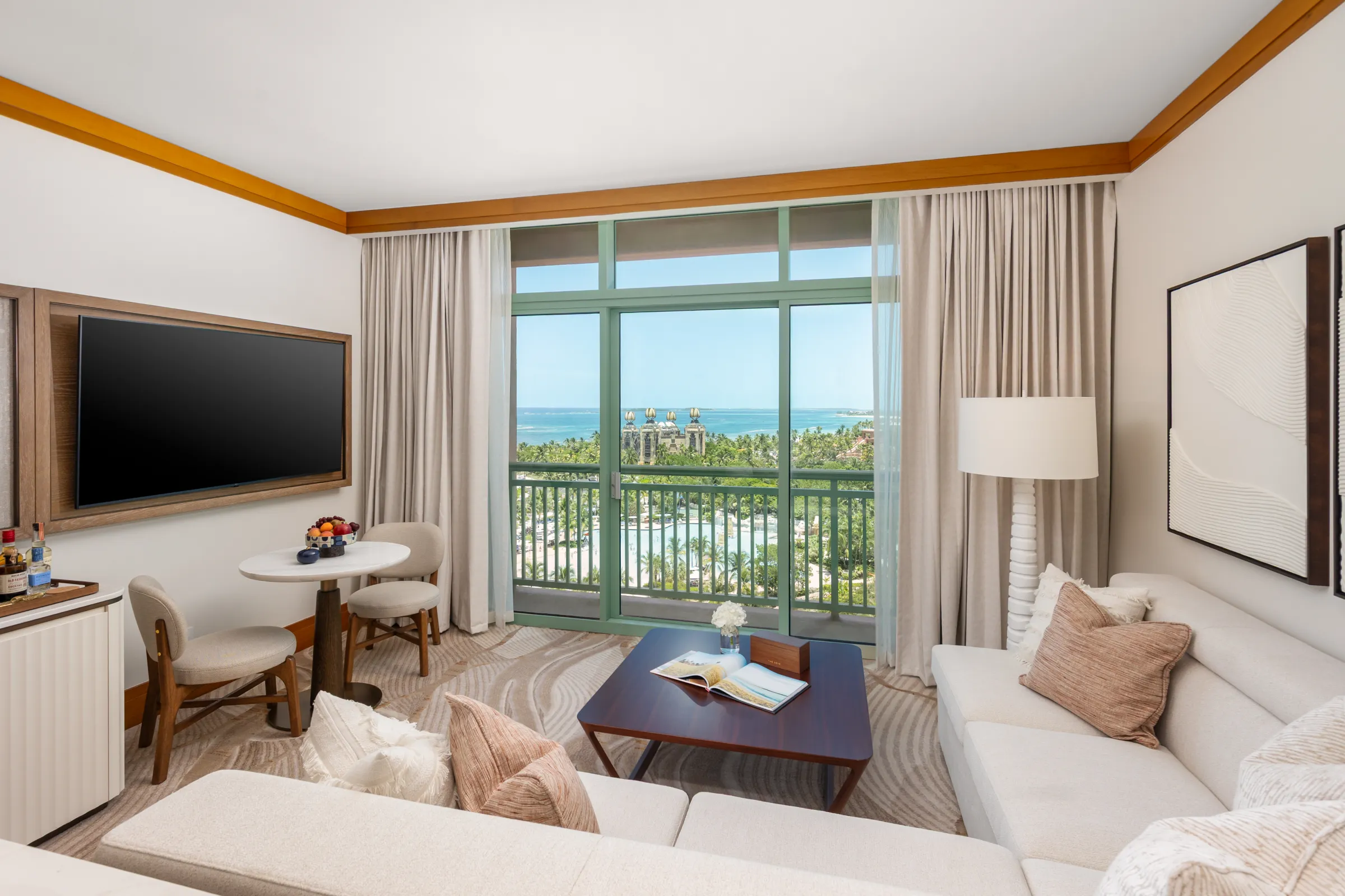 A suite sitting room with a wall-mounted television and terrace doors open to the ocean